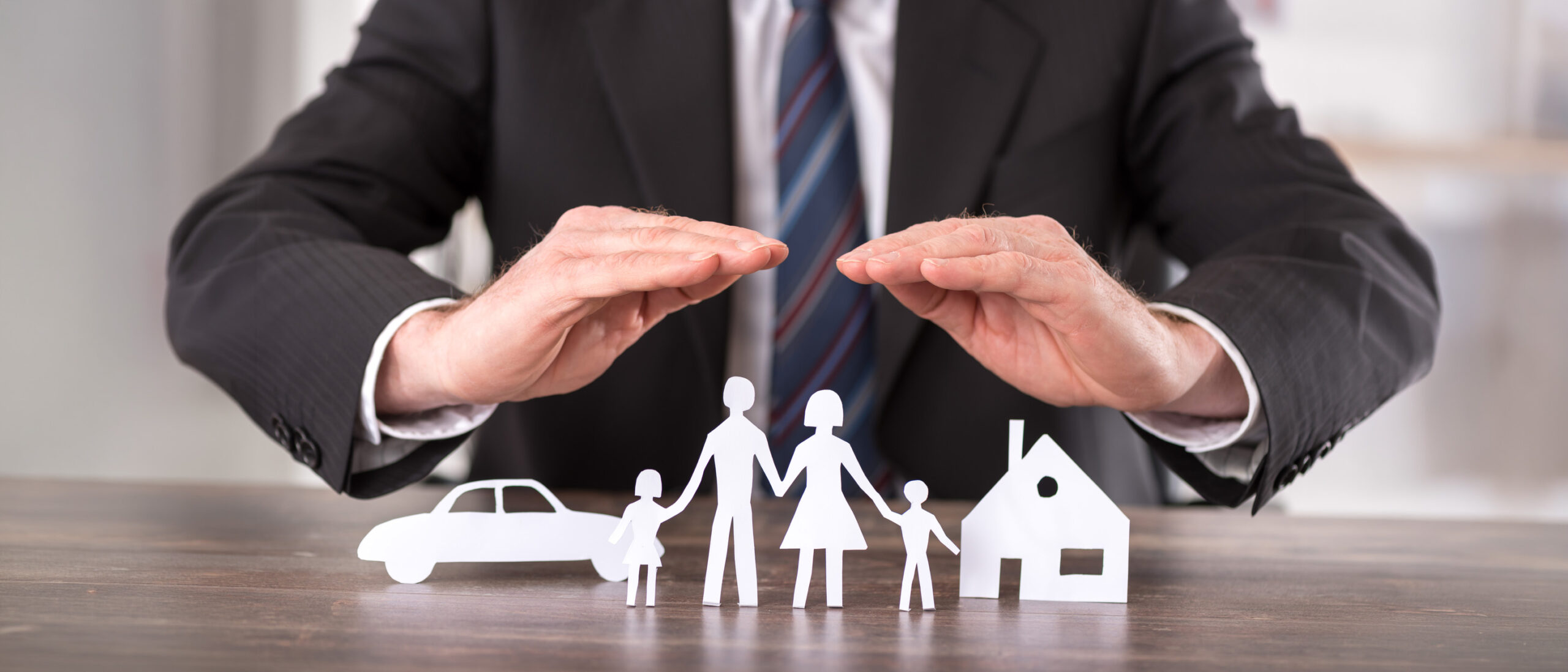 Concept of insurance with hands over a house, a car and a family